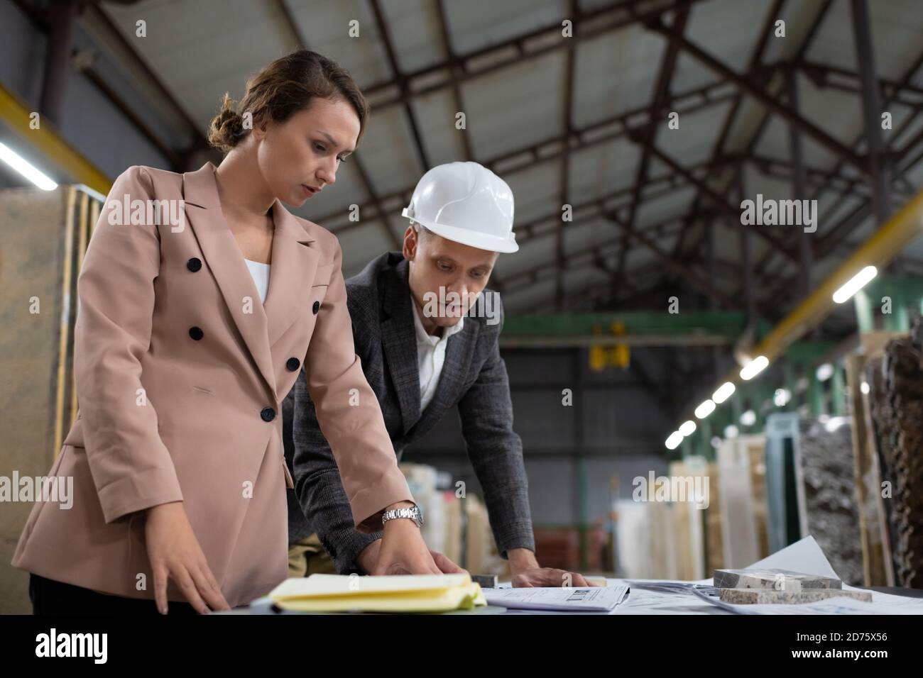 Side view of adult businesspeople at table in storage of marble discussing plan in team Stock Photo