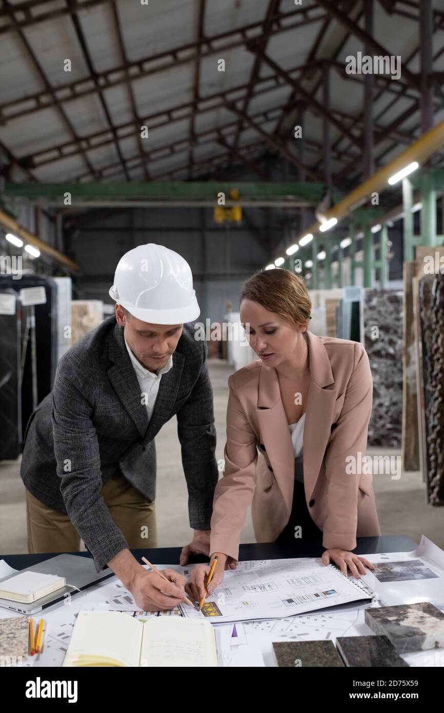 Adult professional workers of stone company examining blueprint and picking samples of marble in warehouse Stock Photo