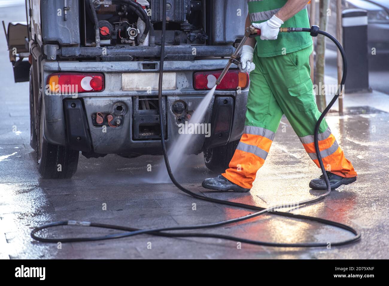 Worker cleaning the streets with a pressurized bleach water gun Stock