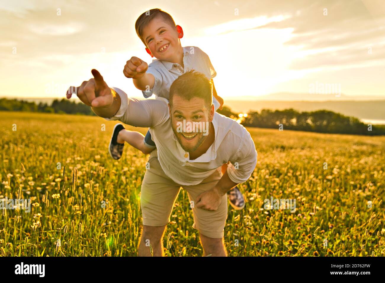 happy family of father and child on field at the sunset having fun on the father back Stock Photo