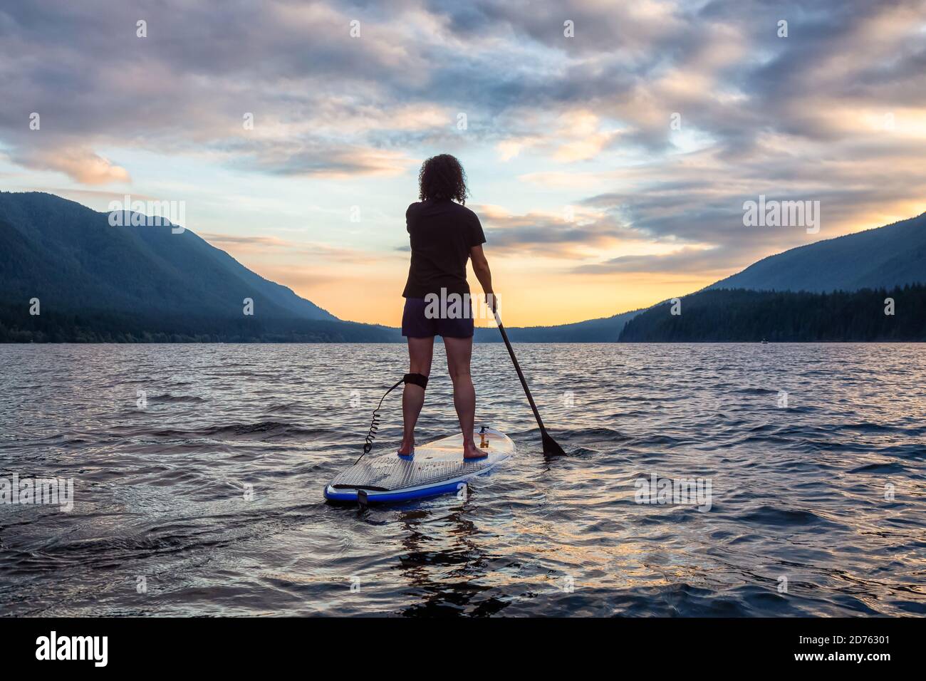 Woman Paddleboarding on Scenic Lake at Sunset Stock Photo