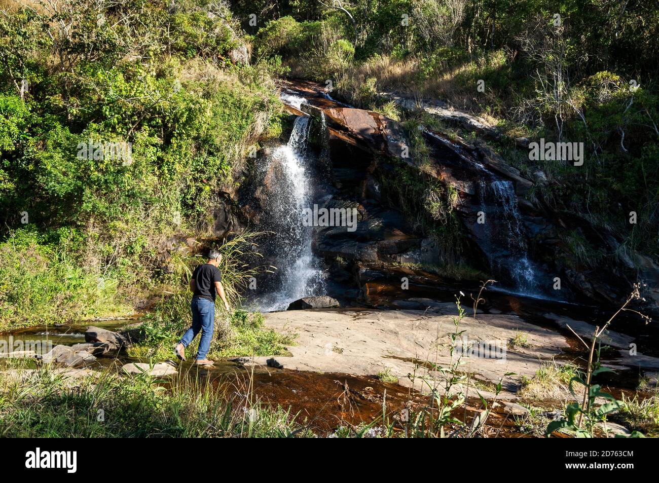 A tourist walking towards Mato Limpo waterfall. This is a roadside cascade located by the Salvador Pacetti road margins in the neighborhood of Cunha. Stock Photo