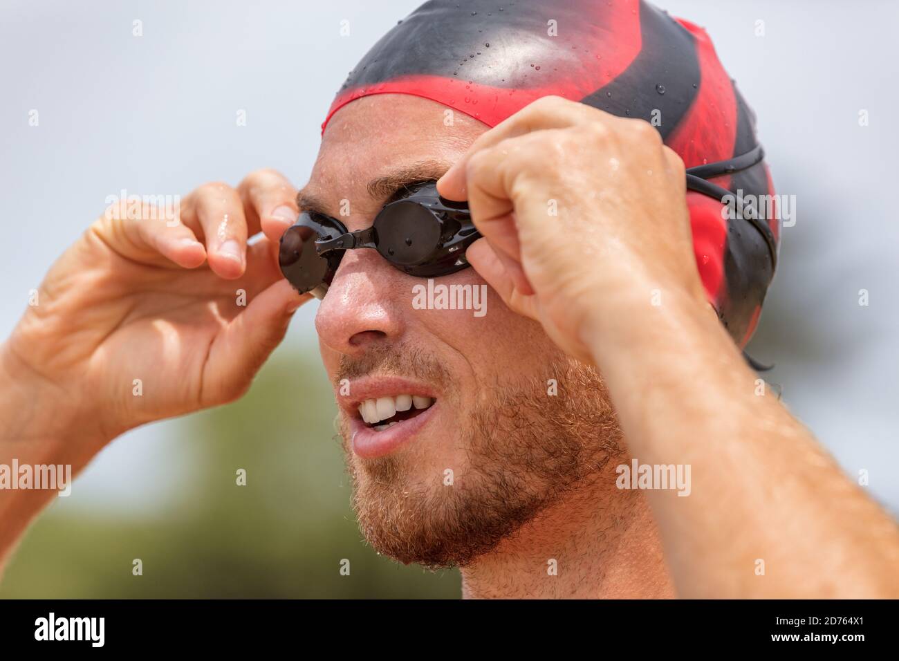 Triathlon swimmer athlete going swimming. Male triathlete swimmer putting swim goggles getting ready for an ocean swim. Fit man in professional Stock Photo