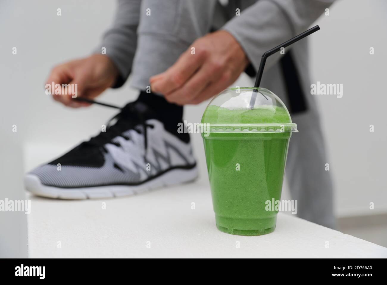 Green smoothie man tying running shoes laces ready to run in urban city. Healthy active lifestyle, closeup of trainers Stock Photo