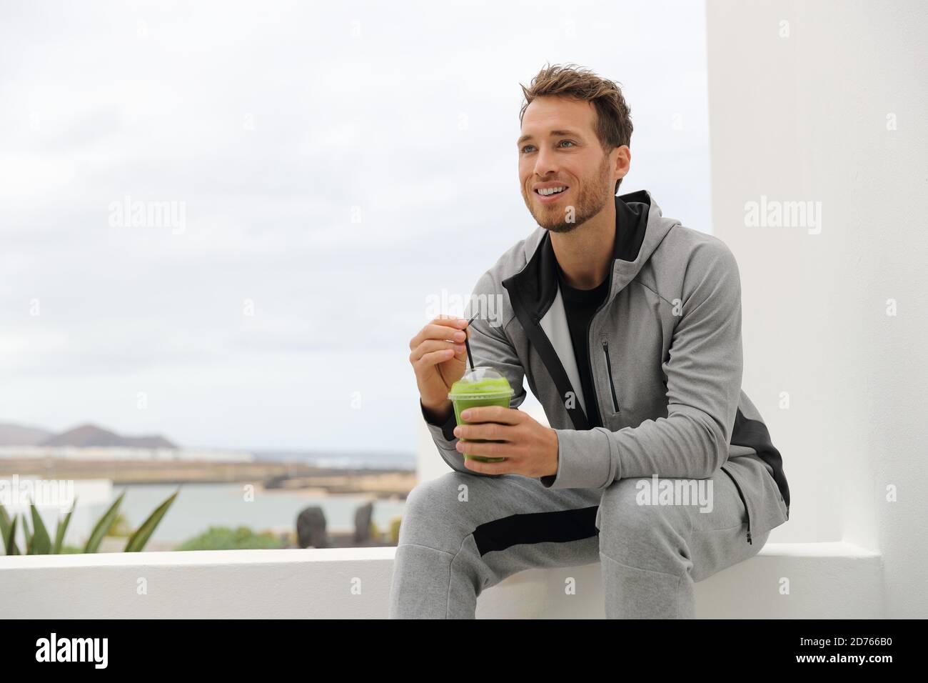 Healthy man drinking green smoothie at home terrace. Sport athlete with spinach cold pressed juice plastic cup drink relaxing outdoors Stock Photo