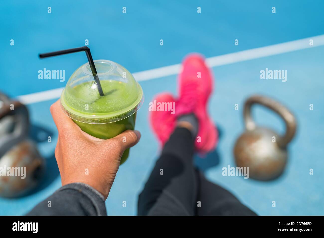 Fitness smoothie weight loss woman taking food selfie of detox green juice with kettlebells at outdoor training gym. Hand holding plastic cup of Stock Photo