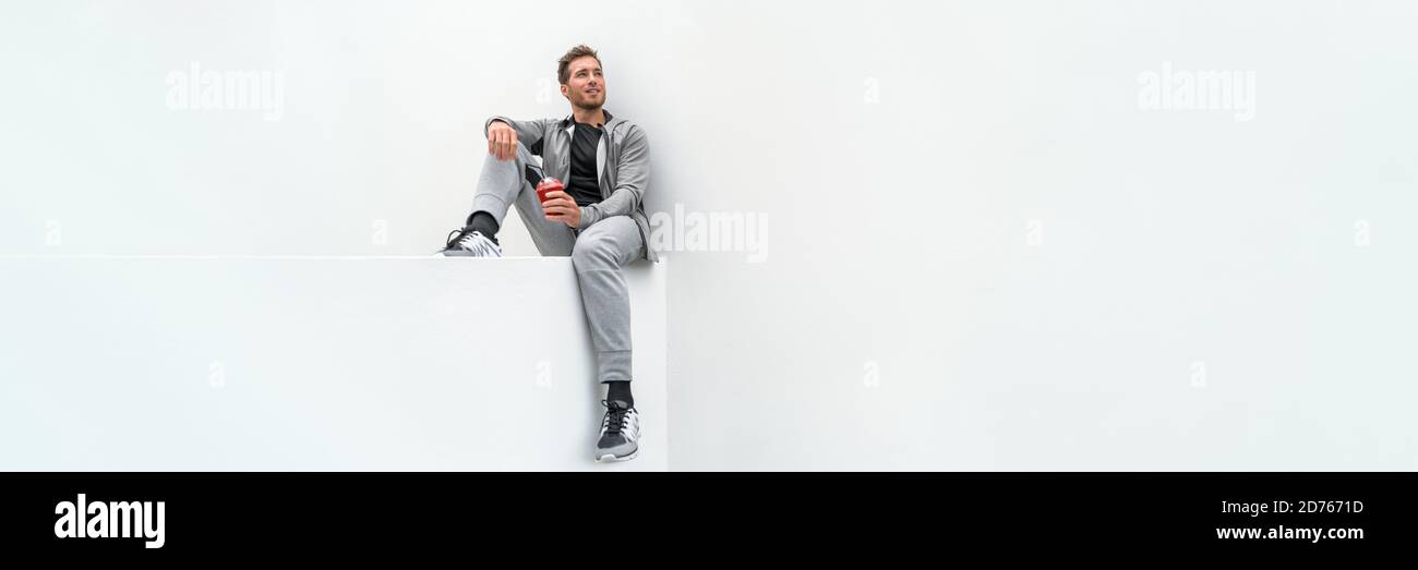 Ftiness sport man drinking smoothie workout banner relaxing at home in gym jogging pants activewear outdoor. Athlete sitting on white background Stock Photo