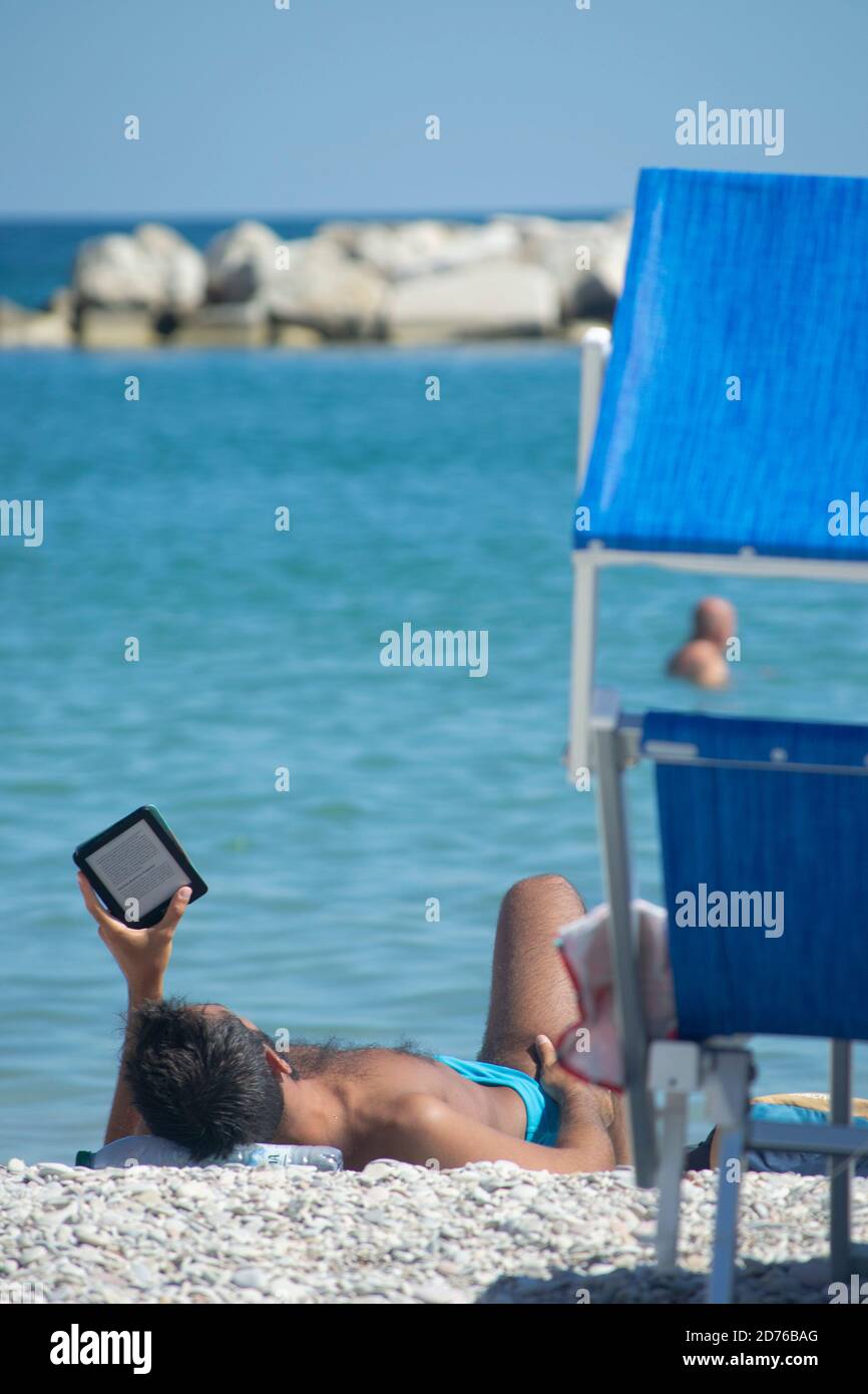 man reads e-book lying on the sand using a plastic bottle as a pillow Stock Photo