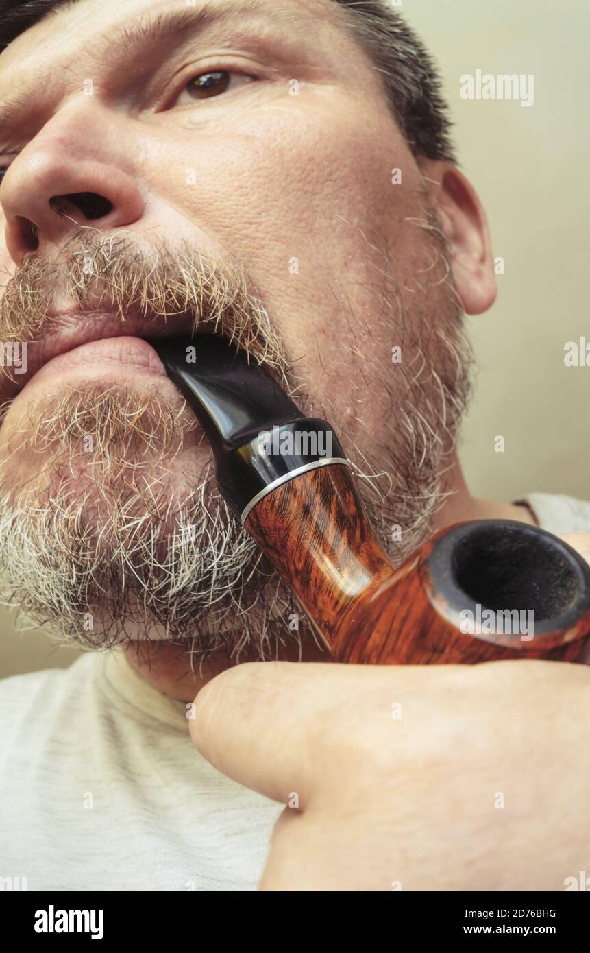 Unusual portrait of a bearded man with a smoking pipe in his mouth. A