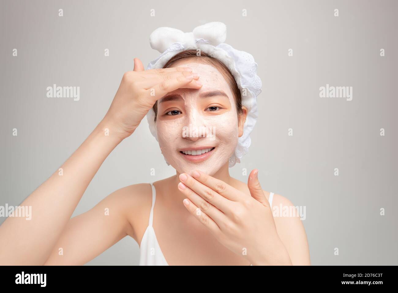 Portrait of confident lady in bathrobe and towel on head with joy while touching her face with clay mask while using anti-aging procedures Stock Photo
