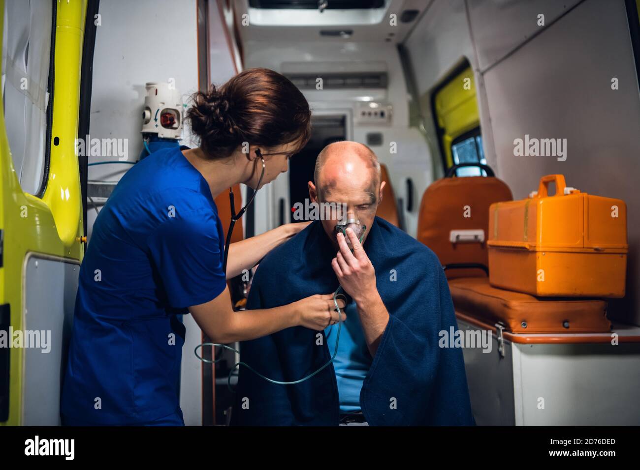A young doctor with a stethoscope is taking care of her injured patient in an ambulance car. Stock Photo