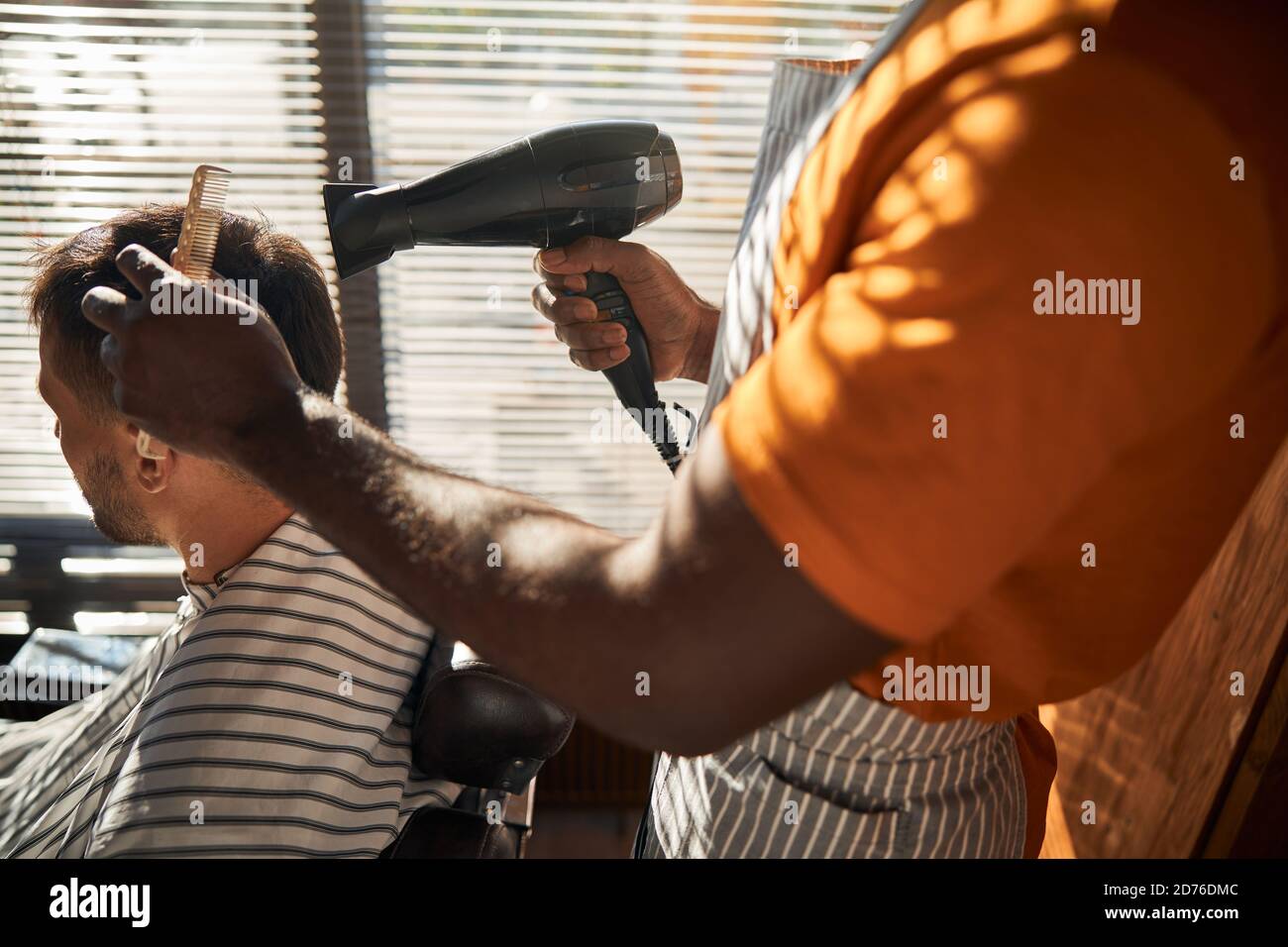 Male barber blow drying client hair in barbershop Stock Photo