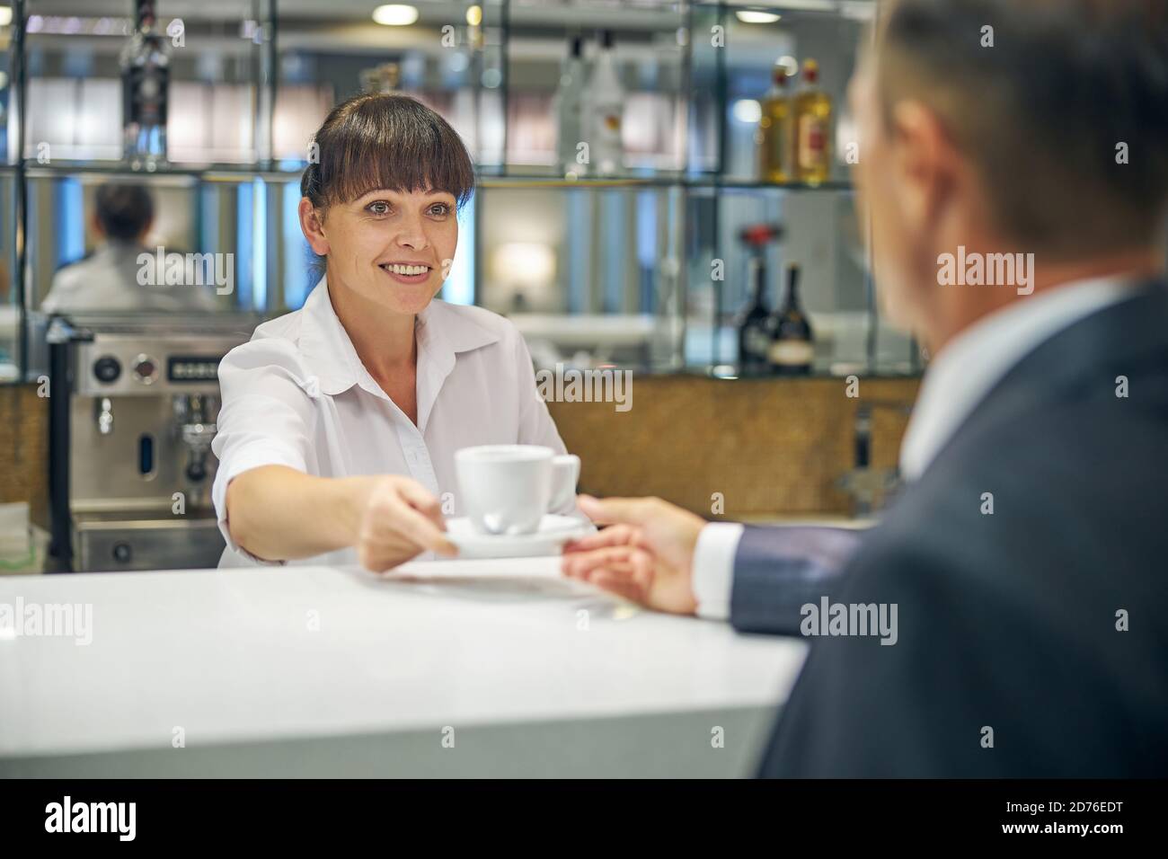 Cheerful barmaid serving male client with hot drink Stock Photo