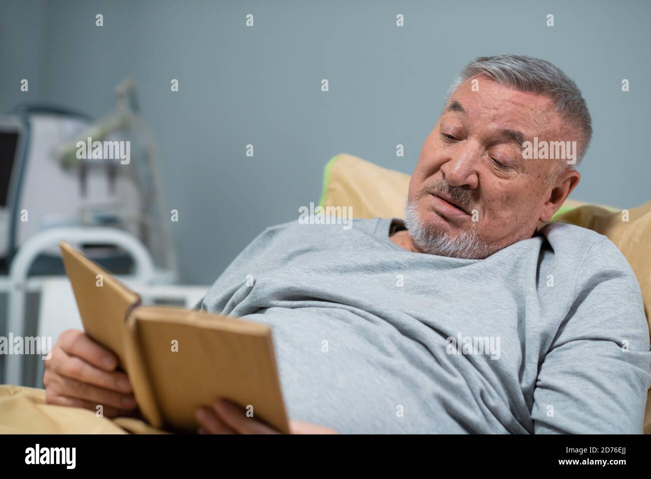 A male patient in his mid sixties reading a book in a hospital ward. Stock Photo