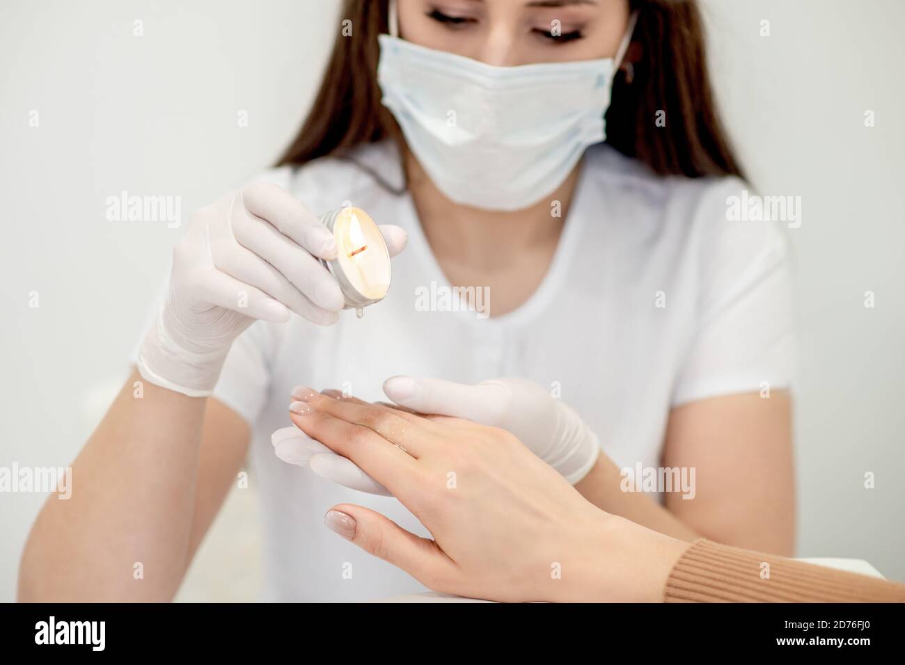 Manicure master applying warm wax from candle on fingernails of young