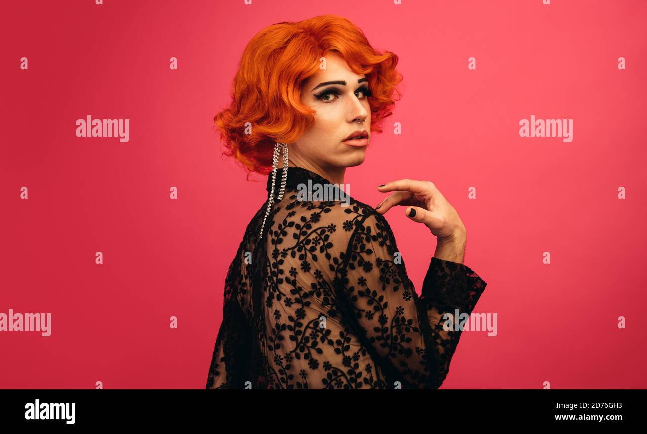 Man dressed as woman looking over his shoulder. Glamarous drag queen against red background. Stock Photo