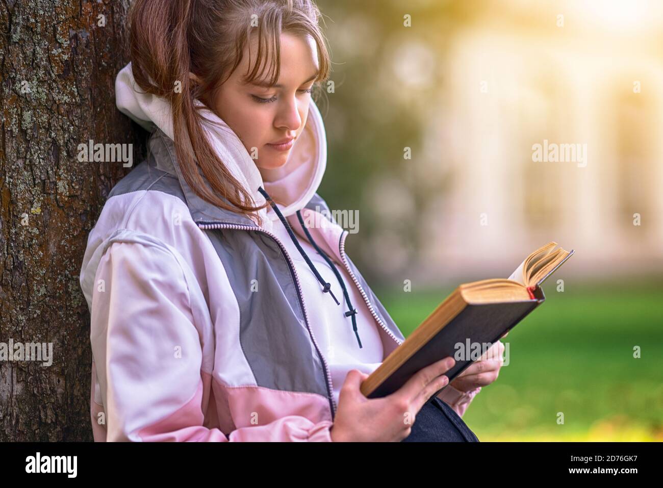 Pretty young teenage girl sitting reading a book or studying outdoors ...