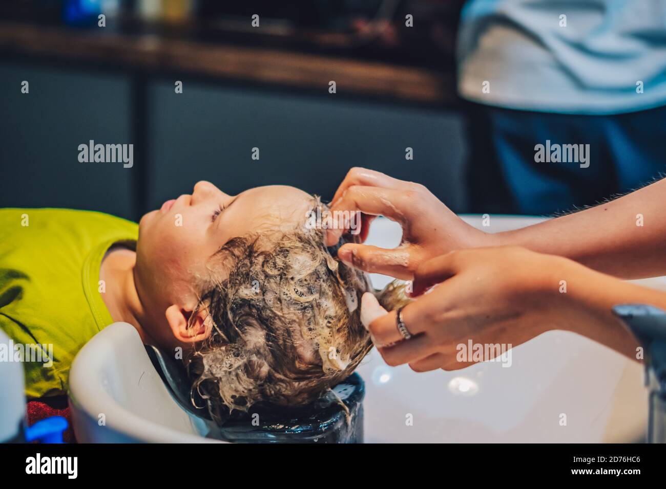 Wet Head White Blond little Boy lie leaning on over sink. Woman female hands. Hair wash massage, Shampoo foam, beauty hairdressing salon. Hairdresser Stock Photo