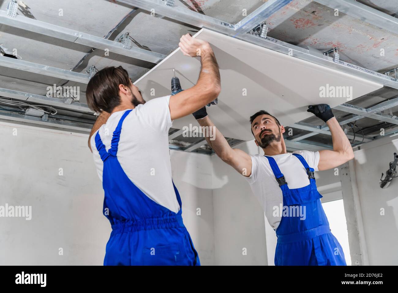 Adjusters in blue overalls stand on a ladder and make a ceiling Stock Photo