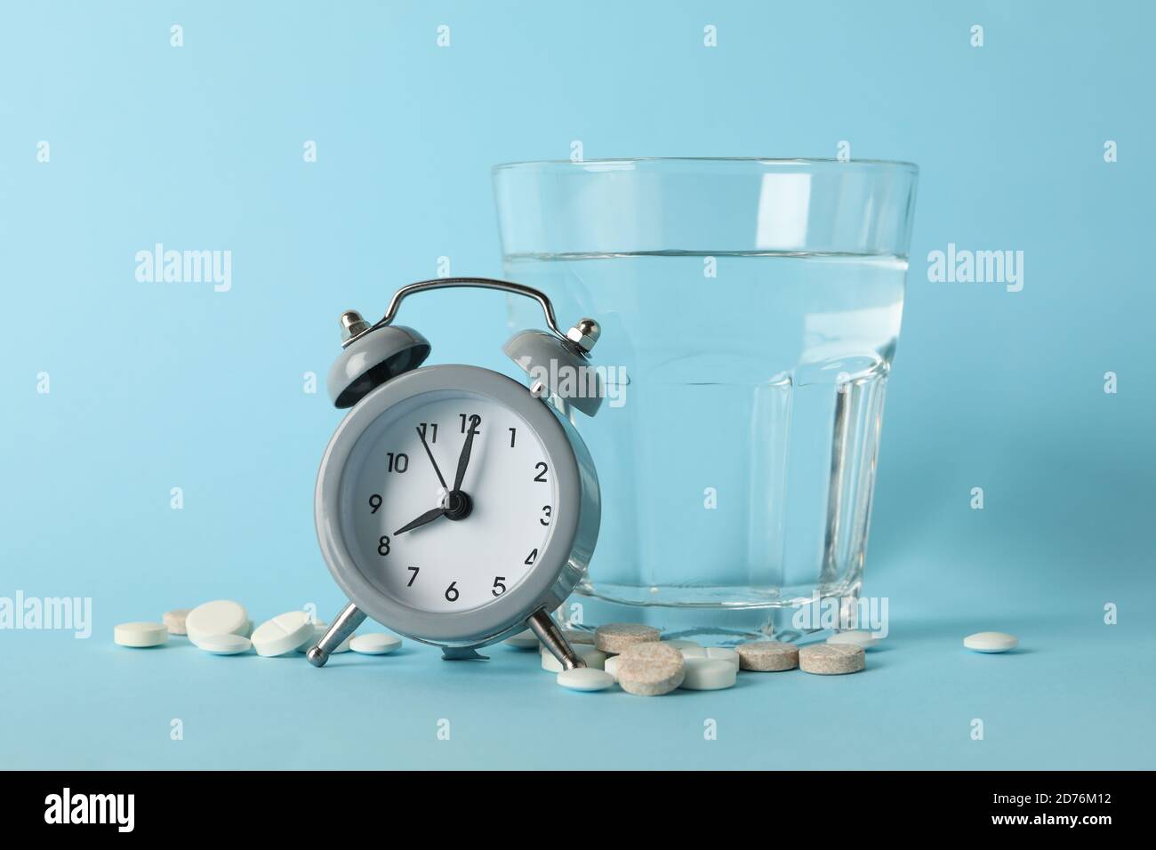 Glass of water, alarm clock and pills on blue background Stock Photo