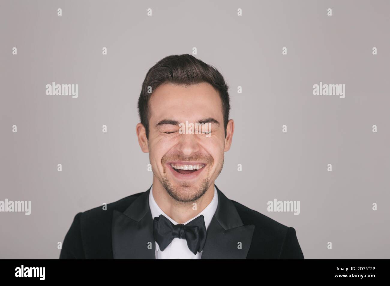 Studio portrait of a young caucasian man in a tuxedo, laughing out loud ...