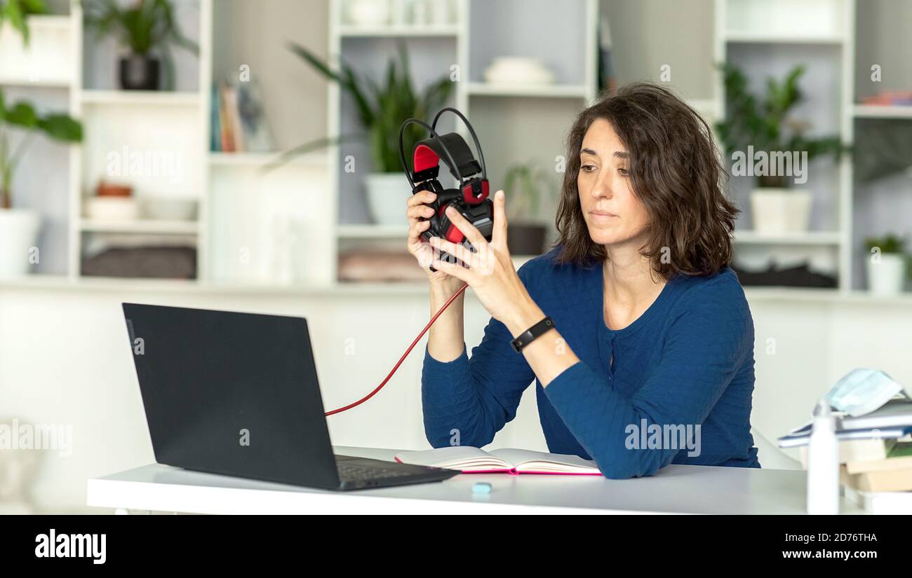 A young brunette woman uses a laptop and headphones in her office or at ...