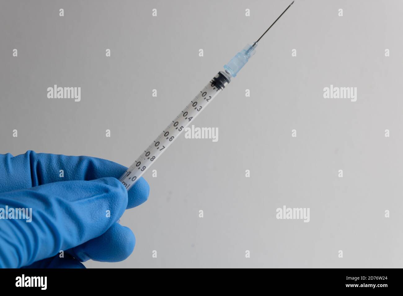 syringe with needle held by a hand protected by a blue insulated glove on a white background Stock Photo