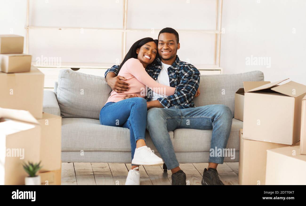 Positive black couple resting on sofa on moving day at their new home, panorama Stock Photo