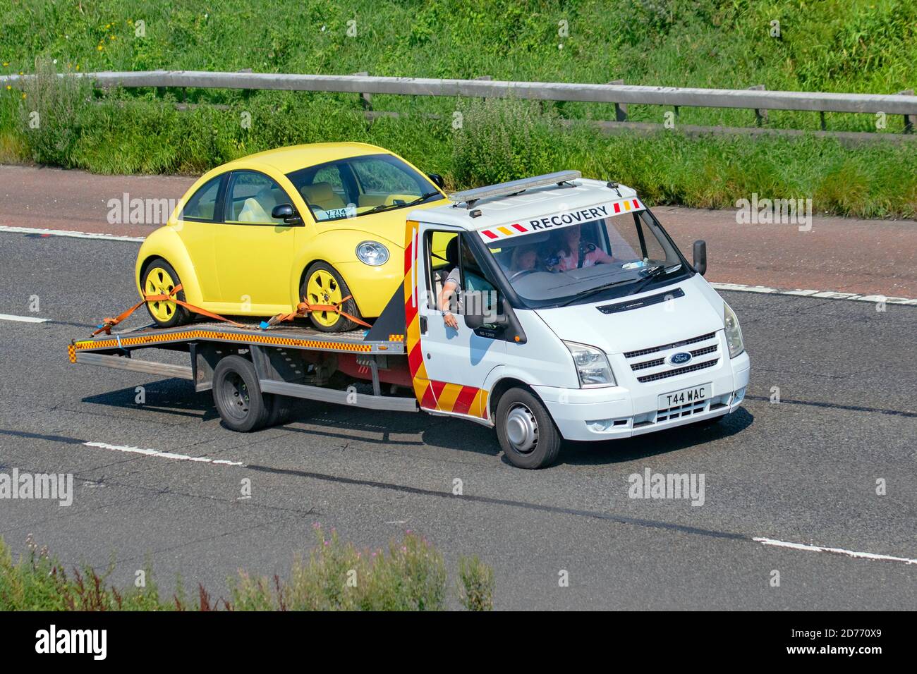 Yellow VW Volkswagen Beetle on car transporter 24 hr breakdown commercial breakdown recovery service;  Haulage delivery trucks, lorry, transportation, truck, cargo carrier, Ford 90 T30 vehicle, European commercial transport, industry, M6 at Manchester, UK Stock Photo