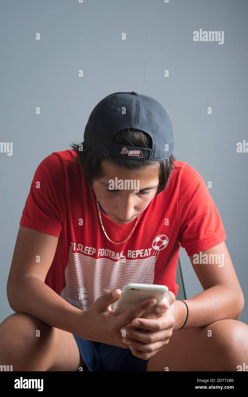Teenage boy in wearing red t-shirt and baseball hat on his phone Stock Photo