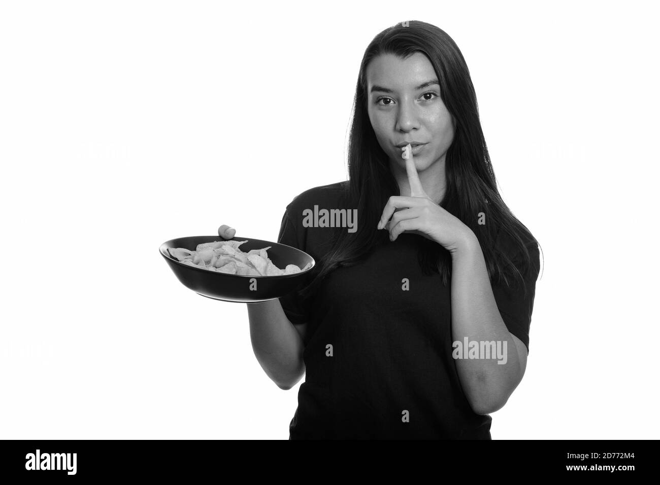 Young beautiful Caucasian woman holding bowl of potato chips with finger on lips Stock Photo