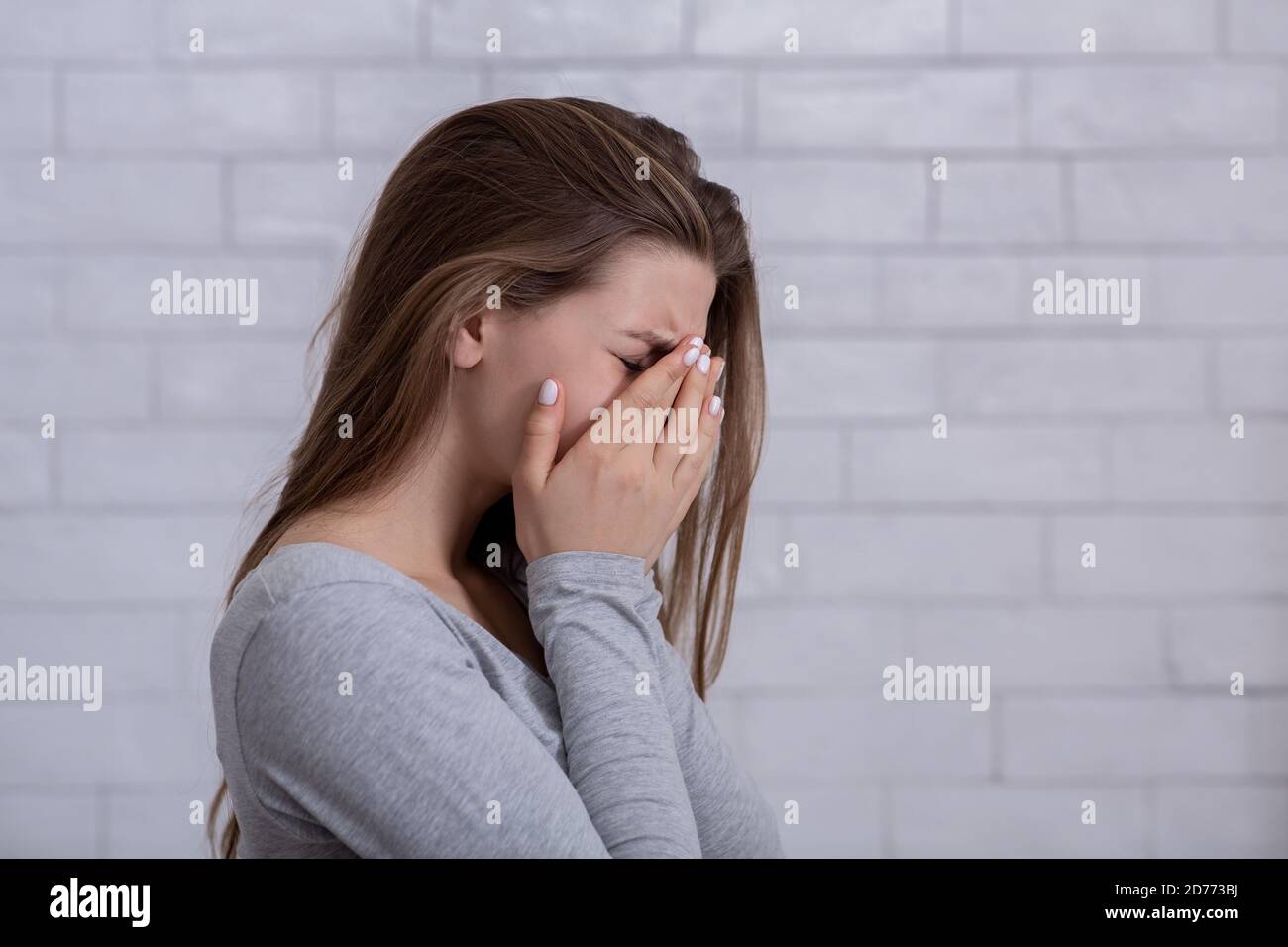 Desperate young woman crying from hopelessness, covering her face with hands, blank space Stock Photo