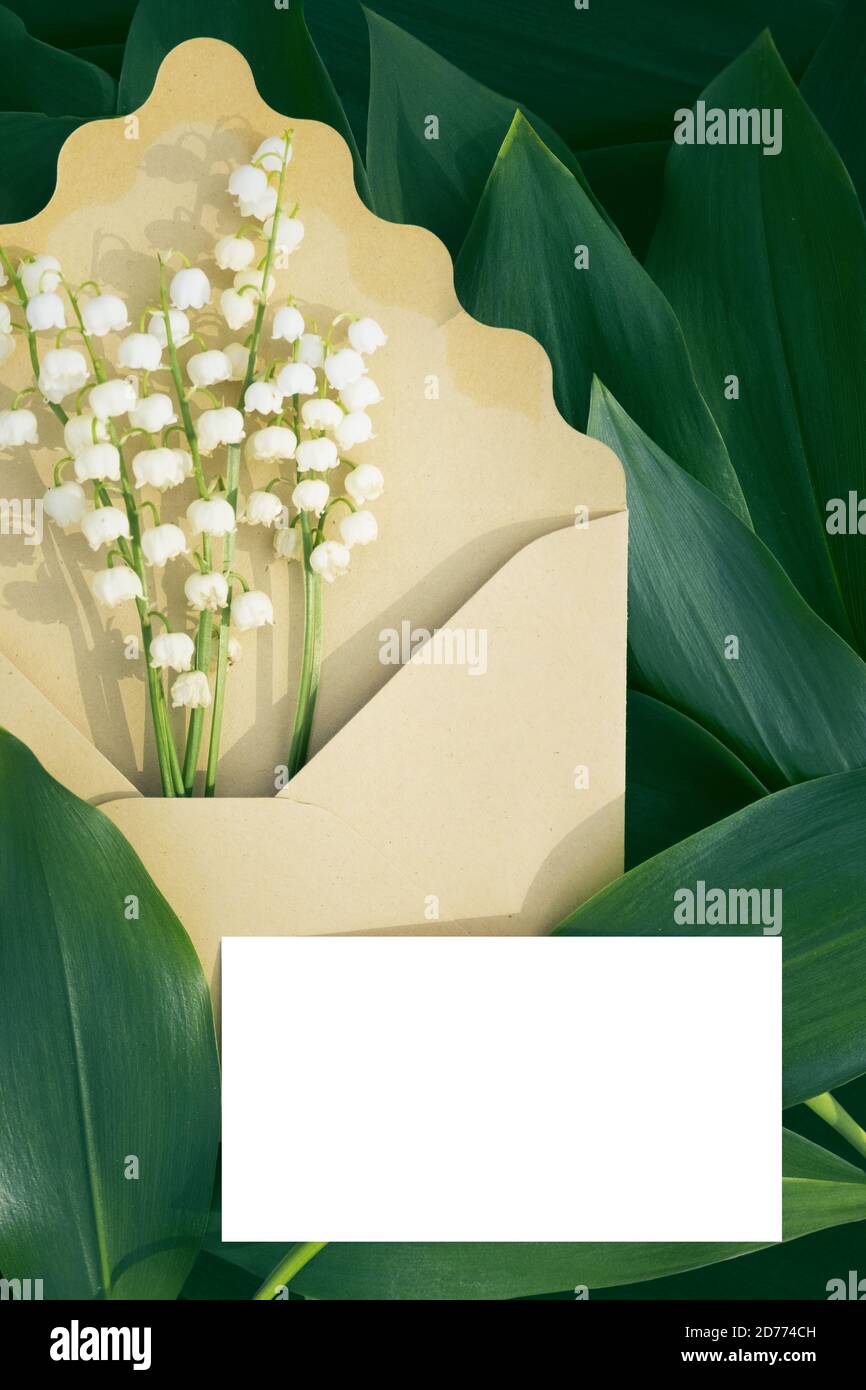 Craft envelope mockup with lily of the valley flower and green leaves on nature ground. May-lily in envelope with business card Stock Photo