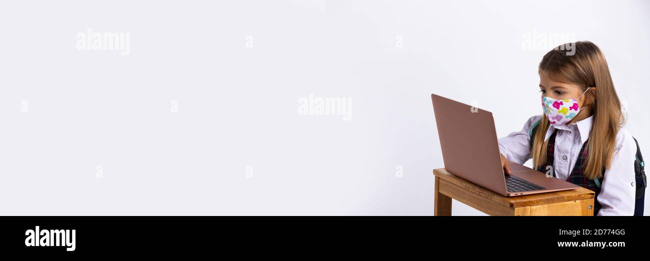 Banner, long format. Online education for children. A schoolgirl is studying the school curriculum using a laptop in a masked mask. Stock Photo