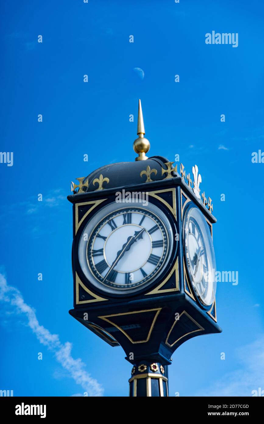 The golden spike decorating the Andrew Fraser Memorial Clock in Colwyn Bay, Wales points to a half moon in a blue sky. Stock Photo