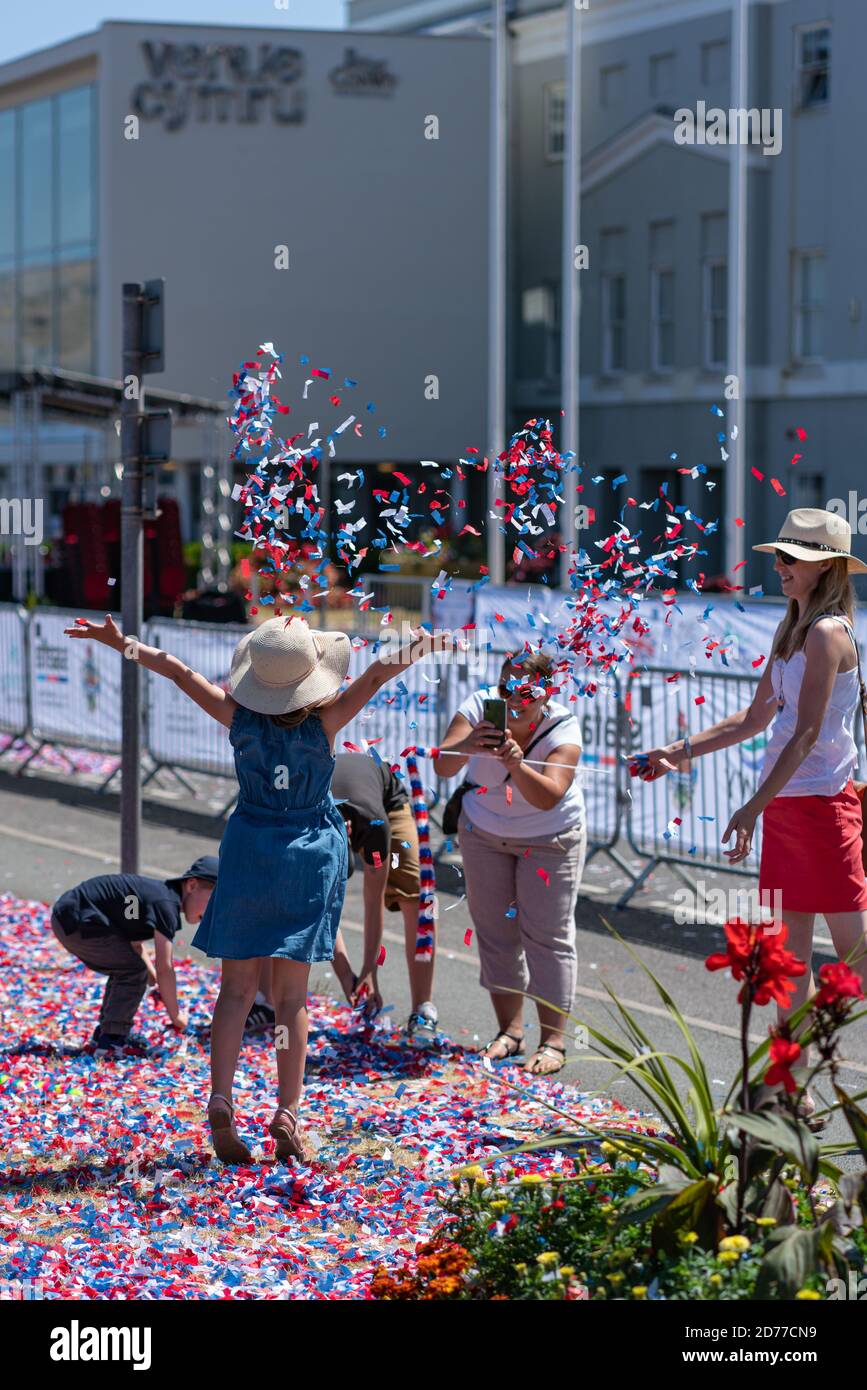 A girl in a sun hat poses for a picture whilst patriotic red, white and blue confetti rains down on her at Llandudno Armed Forces Day Stock Photo