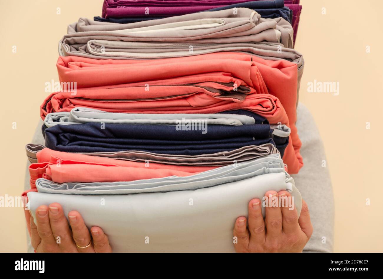 Female hands holding a stack of clean folded linens on a beige background. The concept of housework, washing and ironing. Close-up Stock Photo