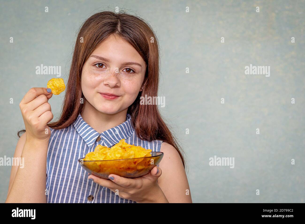 A young girl holds a plate with chips in her hand, chips in the other, smiles and is ready to eat this fast food. Selective focus Stock Photo