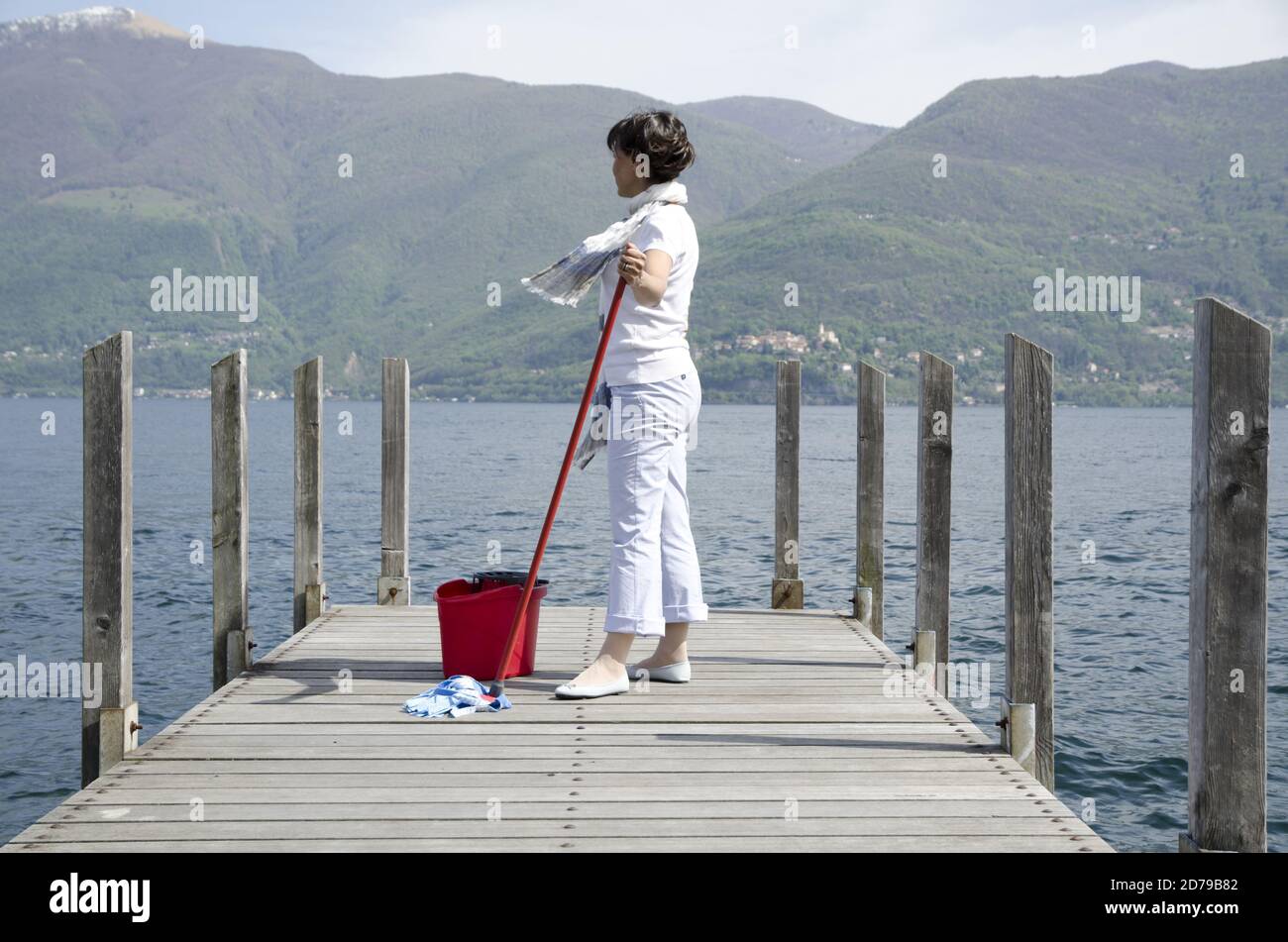 Woman Scrubs the Pier over the Alpine Lake with Cleaning Equipment and  Mountain in Background in Ticino, Switzerland Stock Photo - Alamy