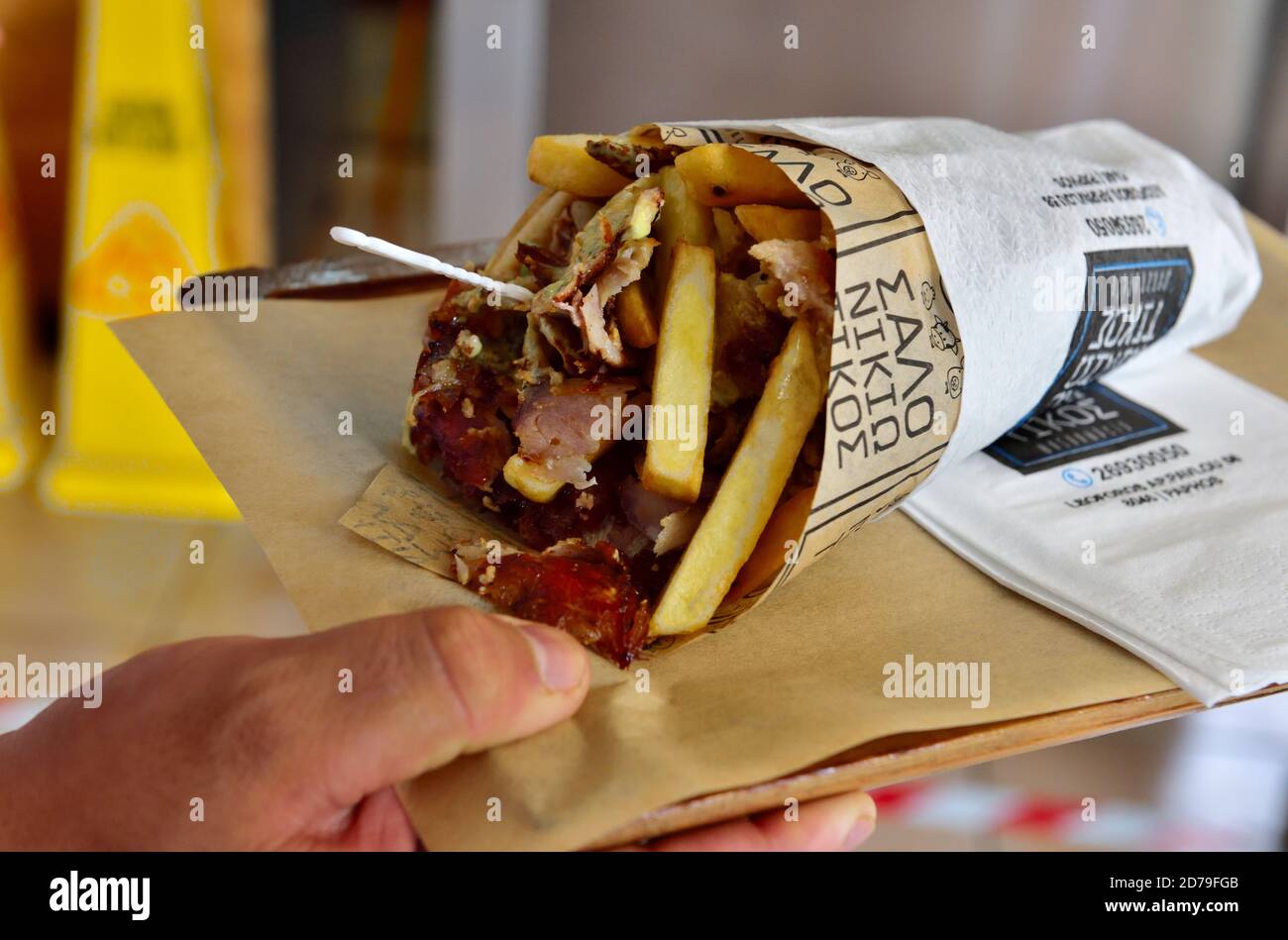 Hand holding platter with a traditional Cypriot giros kebab with meat, salad and potato chips in pitta bread Stock Photo