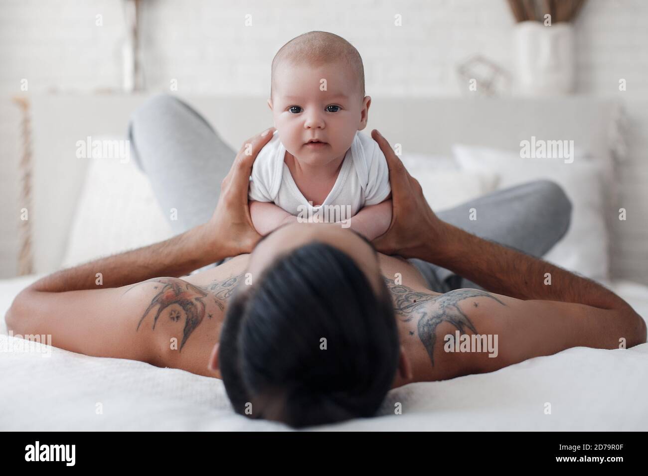 man with infant. happy family at home. happy father with cute two months baby boy laying in light bed at home Stock Photo