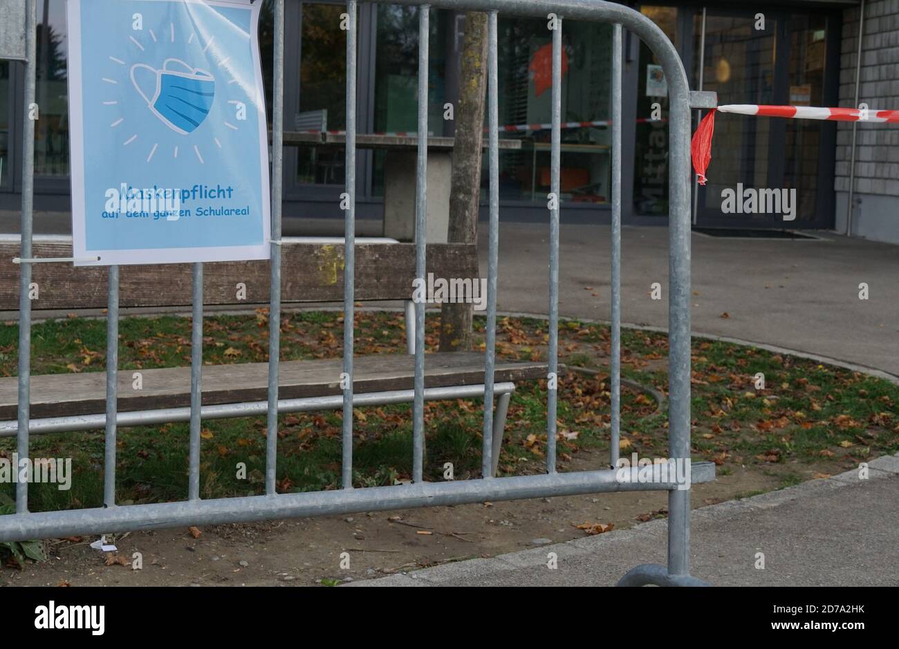 A sign poster in German language saying a face mask is obligatory on school ground, fixed on a metal barrier and a barrier tape in red and white. Stock Photo