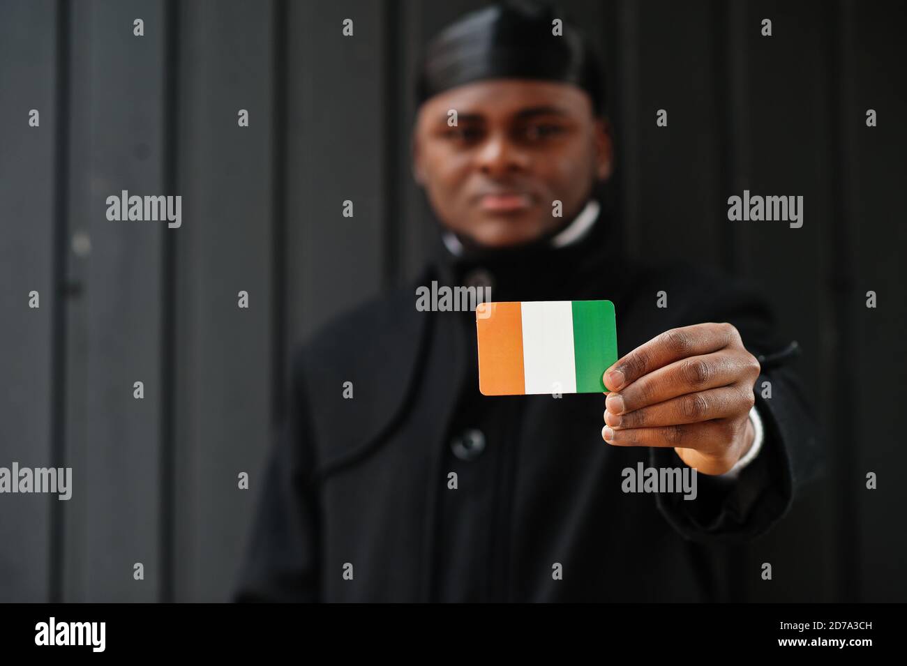 African man wear black durag hold Ivory Coast flag at hand isolated dark background. Stock Photo