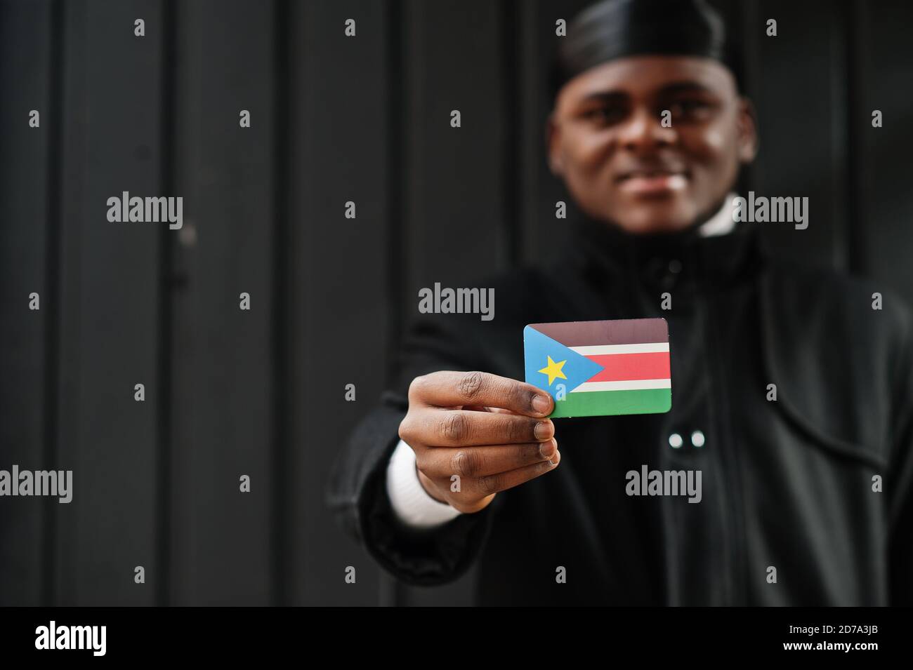 African man wear black durag hold South Sudan flag at hand isolated dark background. Stock Photo