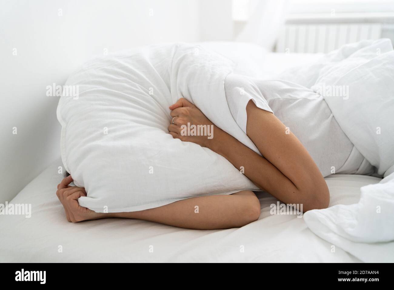 Depressed woman lying alone on bed covering head with pillow feeling afraid or depressed suffer from insomnia, loud sounds of neighbors, has mental pr Stock Photo