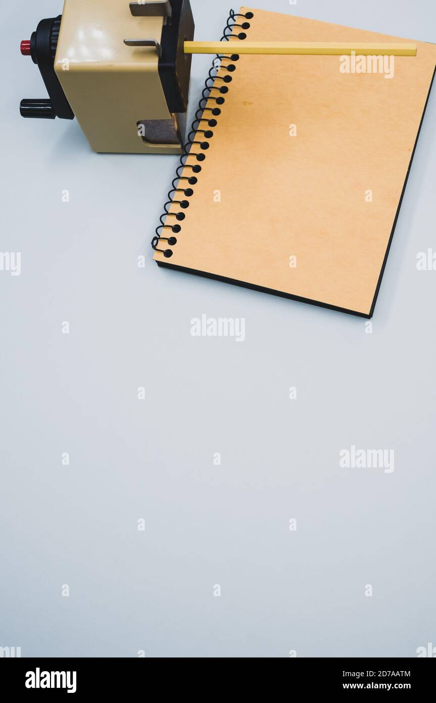 Vertical shot of a notebook and a mechanical pencil sharpener on a blue surface Stock Photo