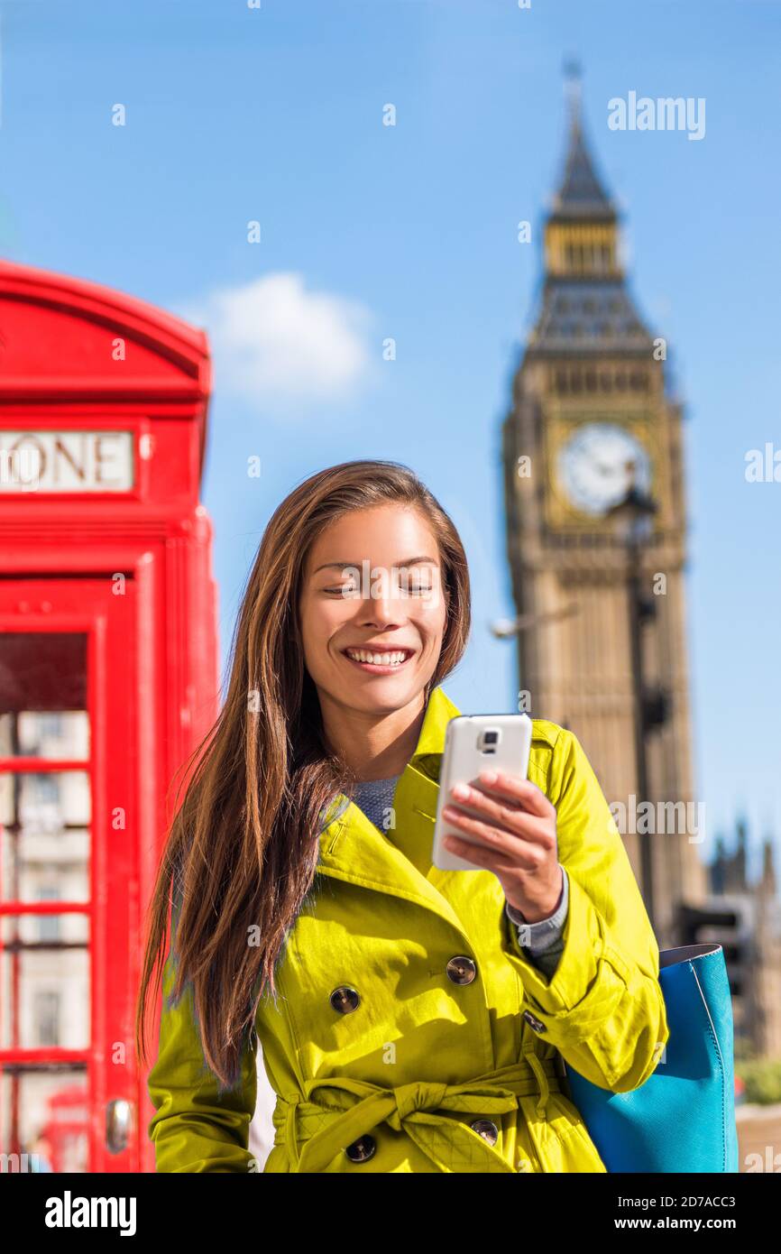 Asian city woman texting on mobile phone walking in London street. Happy chinese girl in yellow spring raincoat outdoors with Big Ben background, UK. Stock Photo