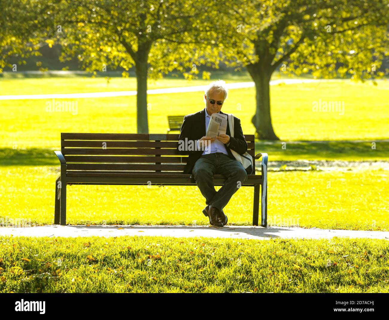 Man relaxes while reading sitting on a park bench in picturesque green park in Cambridge Stock Photo