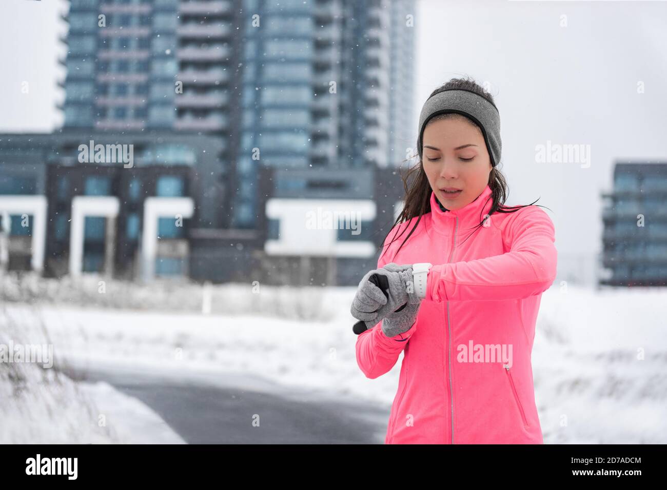 Winter running smartwatch fitness girl in cold snow weather jogging outside on street wearing smart watch and windproof clothes with gloves, headband Stock Photo