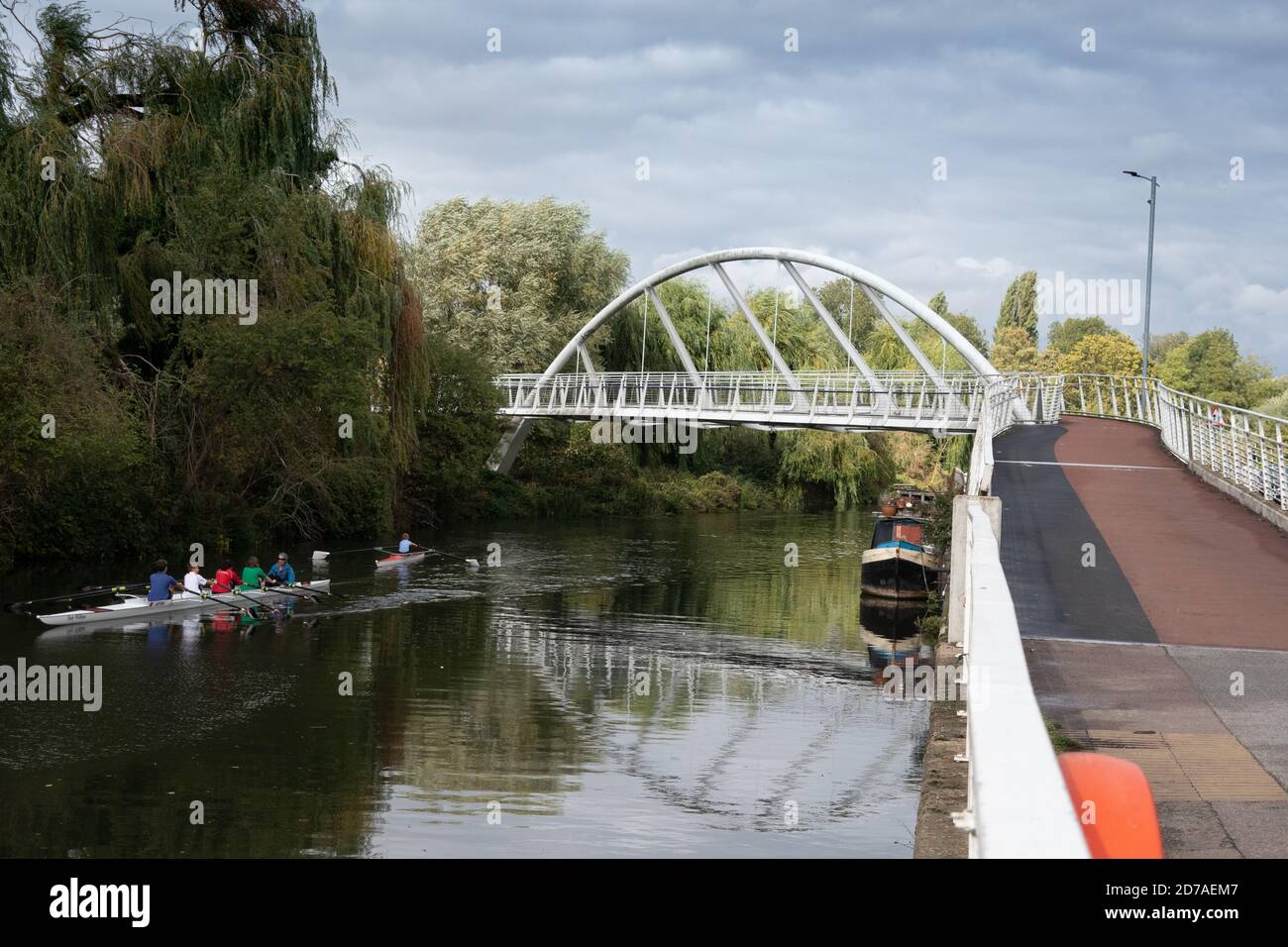 White riverside bridge for walking and cycling. Riverside Bridge on River Cam in Cambridge showing rowers and Canal boats moored Stock Photo